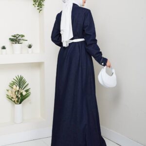 Back view of a navy denim maxi dress with long sleeves, a white waist belt, and contrast hem stitching