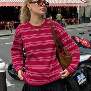 Model wearing a bright pink sweatshirt with white horizontal stripes, a crew neck, and relaxed long sleeves.