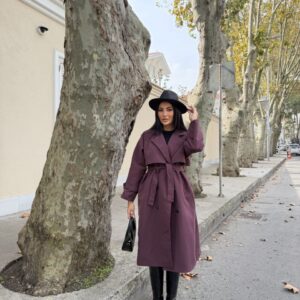 Long plum trench coat with a tied belt, wide lapels, black buttons, and loose cuffed sleeves.