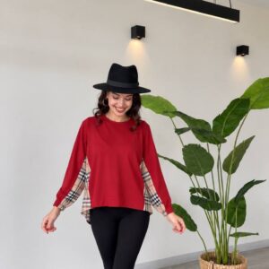 Front view of a red long-sleeve top with beige plaid fabric visible beneath the sleeves and sides.