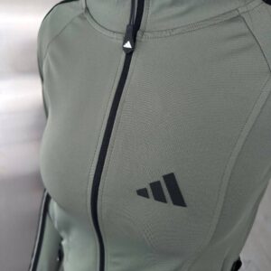 Close-up of a sage high-collar jacket with a black zipper and stitched front panels.