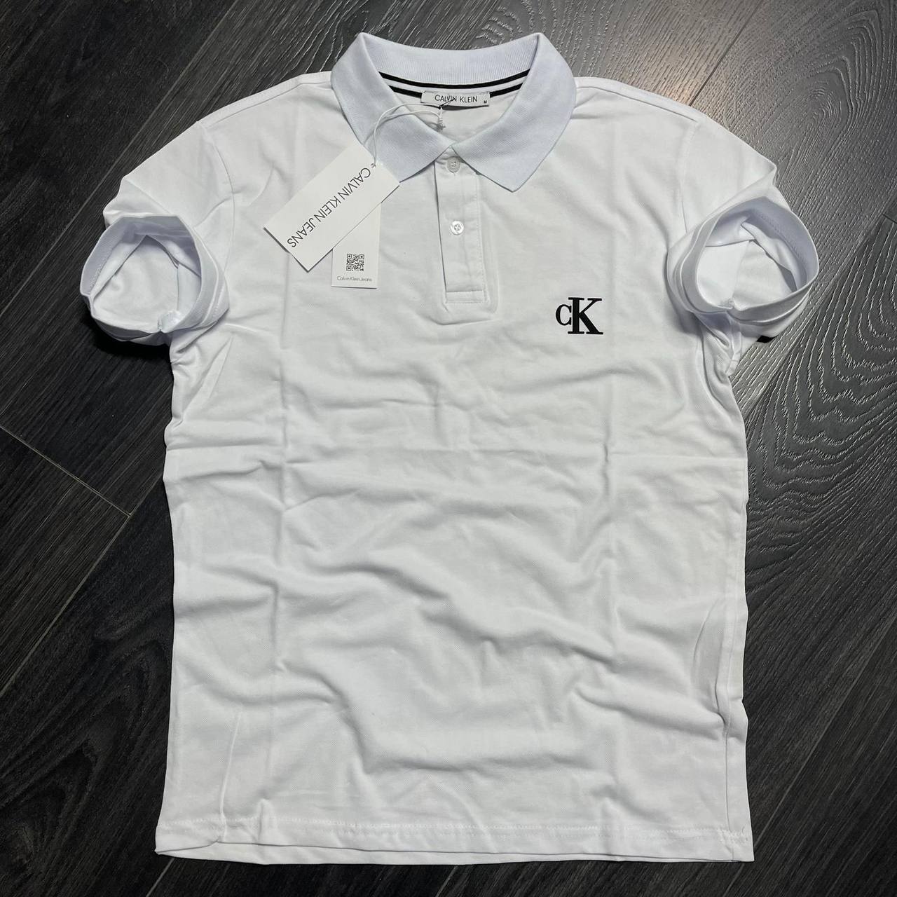 white-polo-front-5831 White short-sleeve polo shirt with a button placket and small black chest emblem, laid flat. available for wholesale in Turkey.