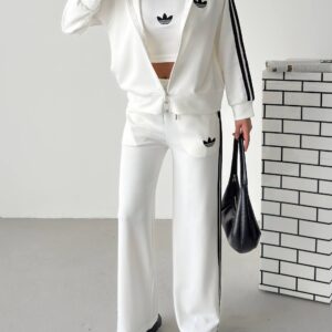 Weiße Reißverschlussjacke und weite Hose mit schwarzen Streifenpanels, kombiniert mit weißem Crop-Top mit schwarzem Ausschnitt.