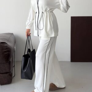 Angled view of a white zip-front tunic and wide-leg trousers with black piping and drawstring waist. available for wholesale in Turkey.