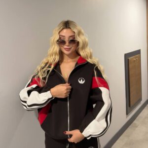 Close view of a black jacket with red shoulder panels, white striped sleeves, elastic cuffs, and a small white chest emblem.
